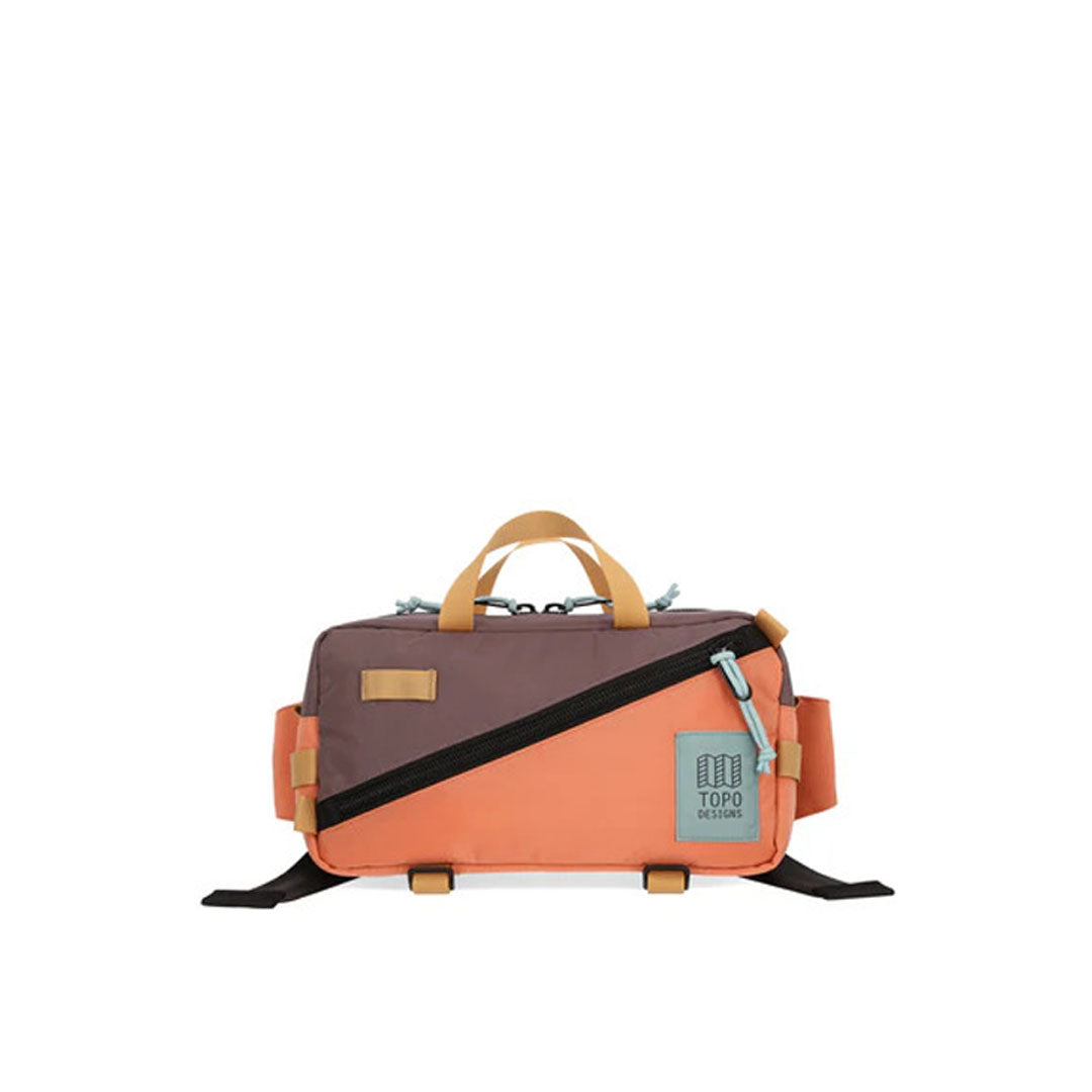 A brown and orange waist pack with a black zipper, branded with 'TOPO DESIGNS', featuring multiple compartments and bottom compression straps.