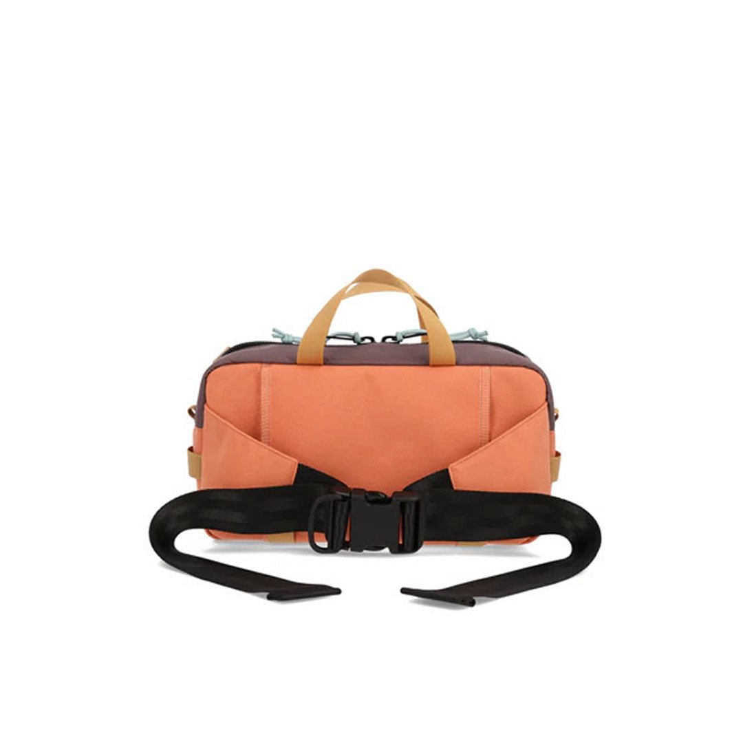 A backside view of a brown and orange waist pack with a black zipper, branded with 'TOPO DESIGNS', featuring multiple compartments and bottom compression straps.